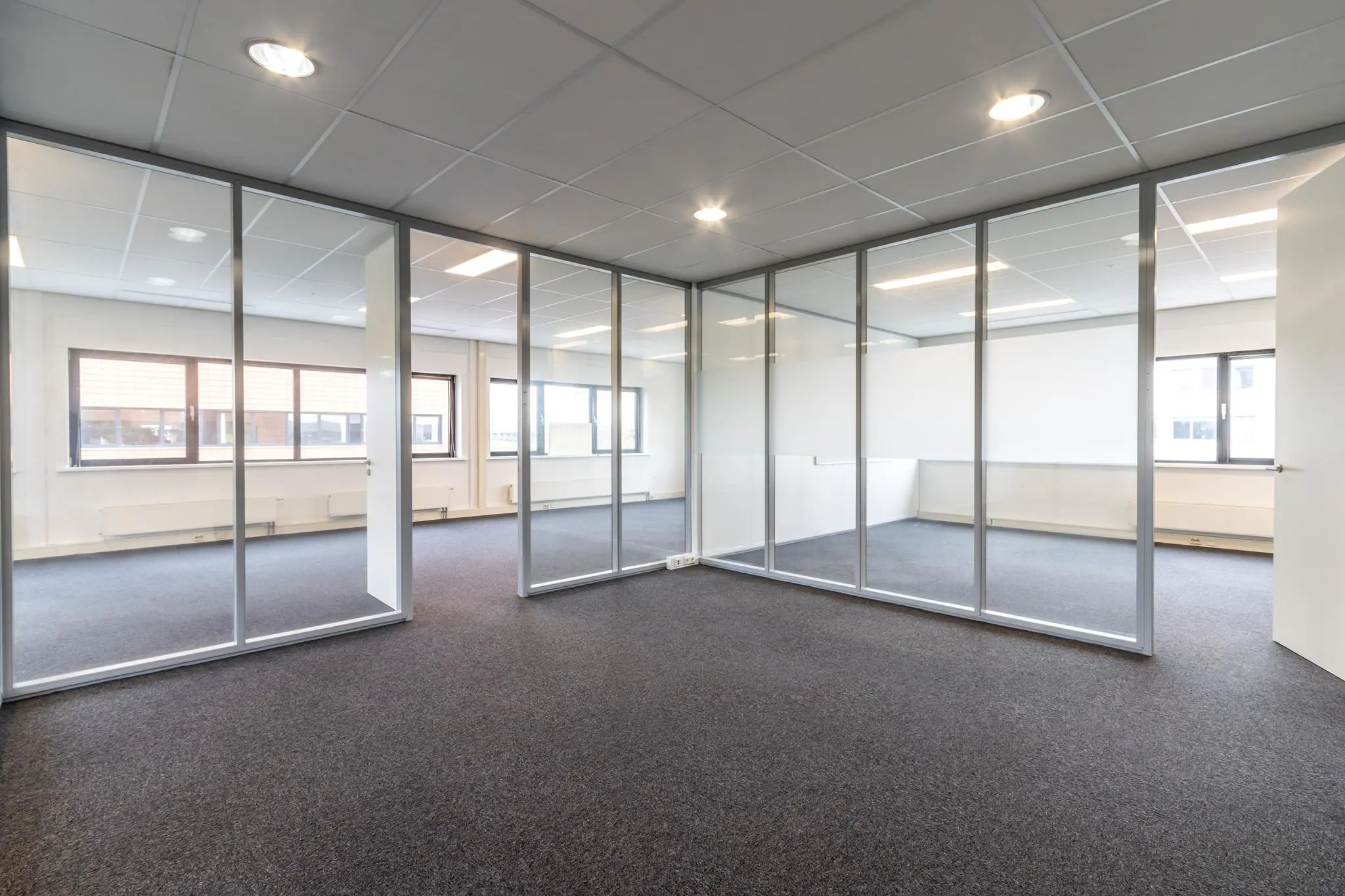 Kantoorruimte aan de Lage Biezenweg met glazen scheidingswanden, systeemplafond en tapijtvloer.